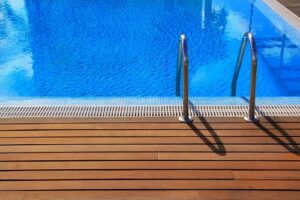 Blue swimming pool with teak wood flooring surrounding.
